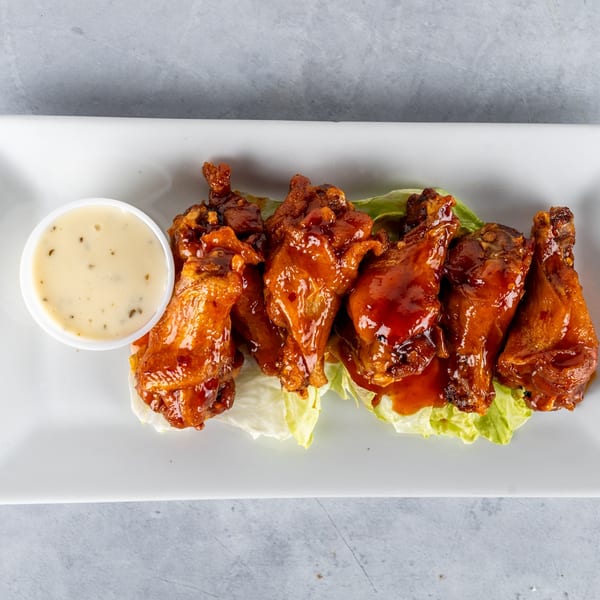 Six glazed chicken wings on a bed of lettuce with a side of ranch dressing.