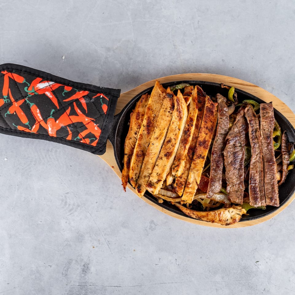 Sizzling Fajitas y Tequila fajitas with grilled chicken and steak, onions, and peppers in a cast iron skillet.