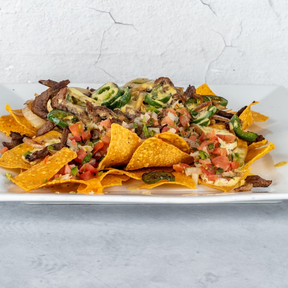 Fajitas y Tequila's steak nachos with jalapeños, pico de gallo, and cheese sauce on a white plate.