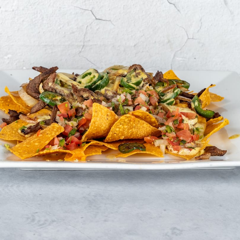 Fajitas y Tequila's steak nachos with jalapeños, pico de gallo, and cheese sauce on a white plate.