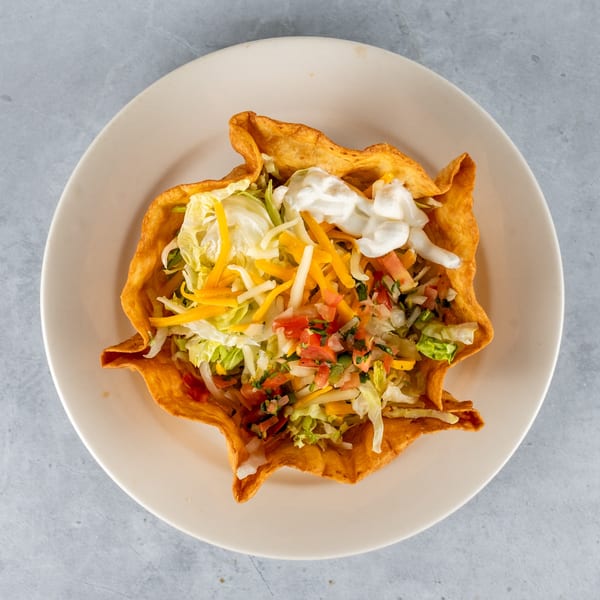A crispy taco salad bowl filled with lettuce, shredded cheese, pico de gallo, and sour cream.