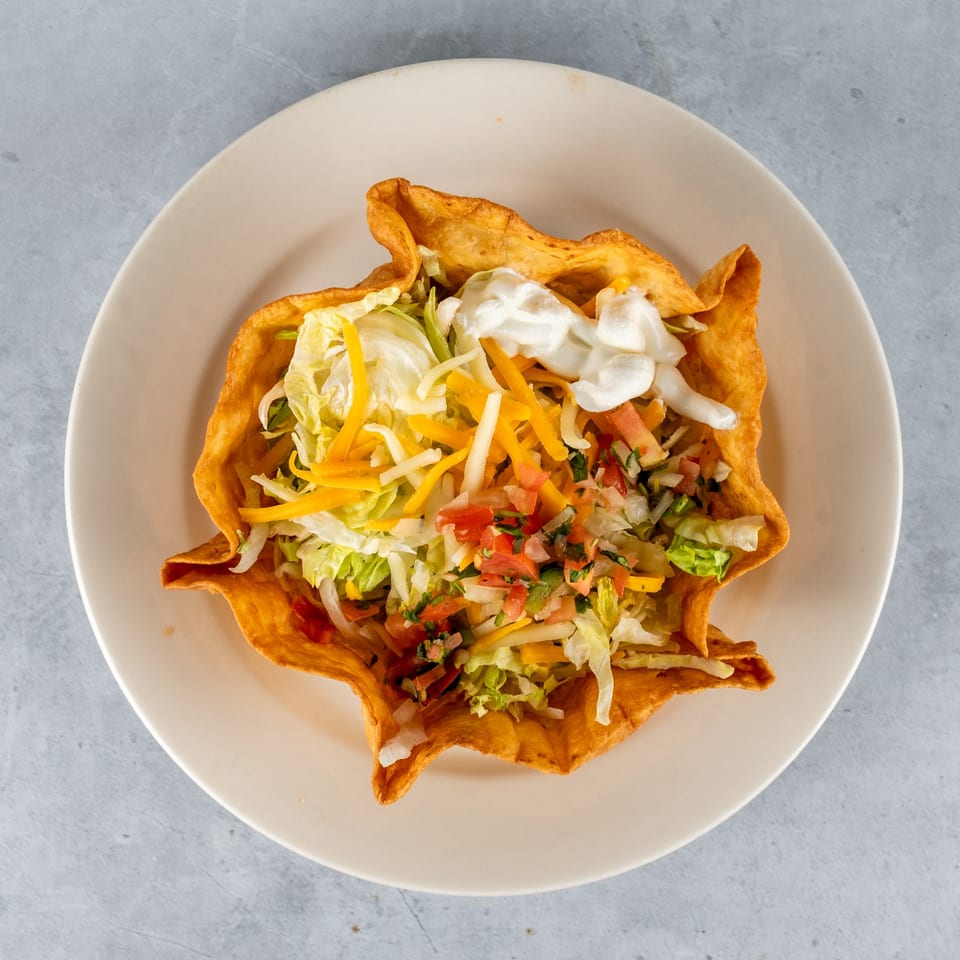 A crispy taco salad bowl filled with lettuce, shredded cheese, pico de gallo, and sour cream.