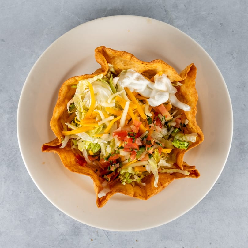 A crispy taco salad bowl filled with lettuce, shredded cheese, pico de gallo, and sour cream.