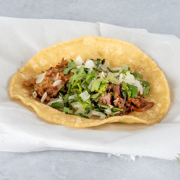 A single Mexican street taco with carnitas, diced onions, and cilantro on a corn tortilla.
