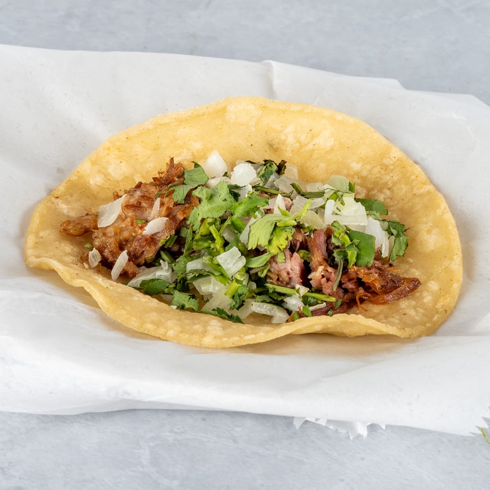 A single Mexican street taco with carnitas, diced onions, and cilantro on a corn tortilla.